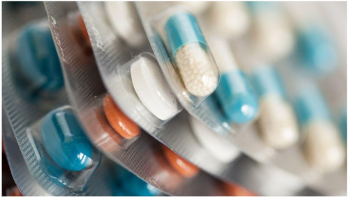 Close-up image of several blister packs containing various types of capsules and tablets, including blue-and-white capsules, white round tablets, and orange round tablets.