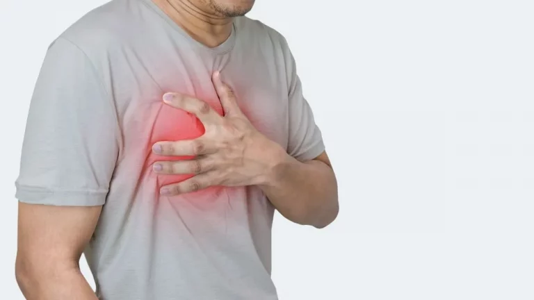 A man in a grey t-shirt clutches his chest, which glows red with pain.